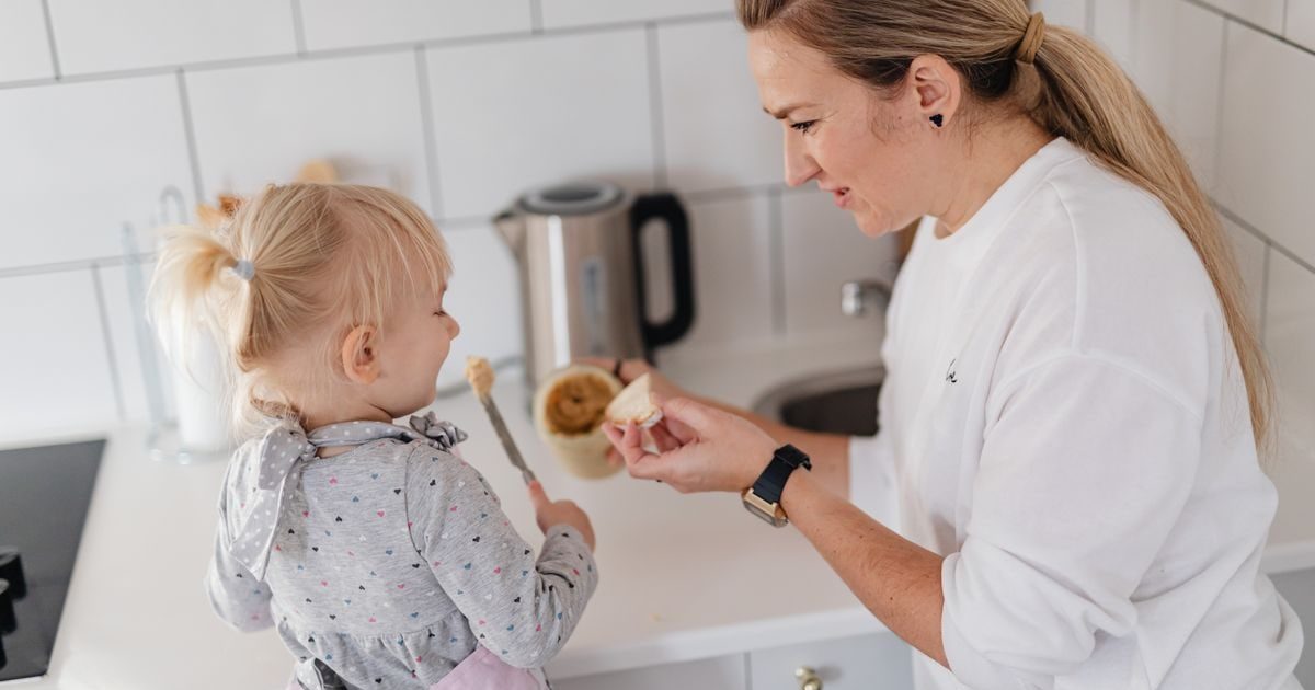 A mother and her young daughter interact while preparing food in a modern kitchen.