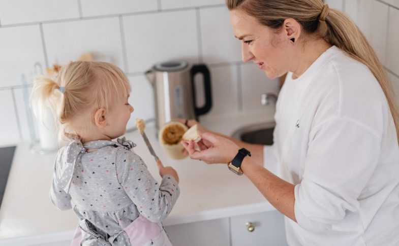 A mother and her young daughter interact while preparing food in a modern kitchen.
