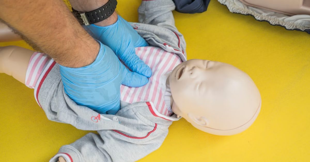 Hands performing CPR on an infant mannequin for a first aid training session.