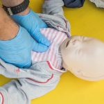 Hands performing CPR on an infant mannequin for a first aid training session.