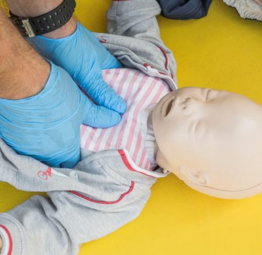 Hands performing CPR on an infant mannequin for a first aid training session.