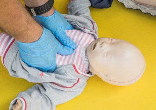 Hands performing CPR on an infant mannequin for a first aid training session.