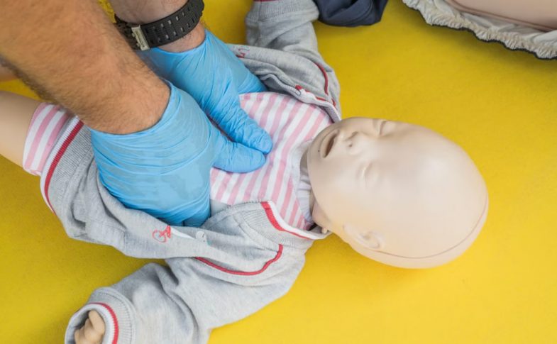 Hands performing CPR on an infant mannequin for a first aid training session.