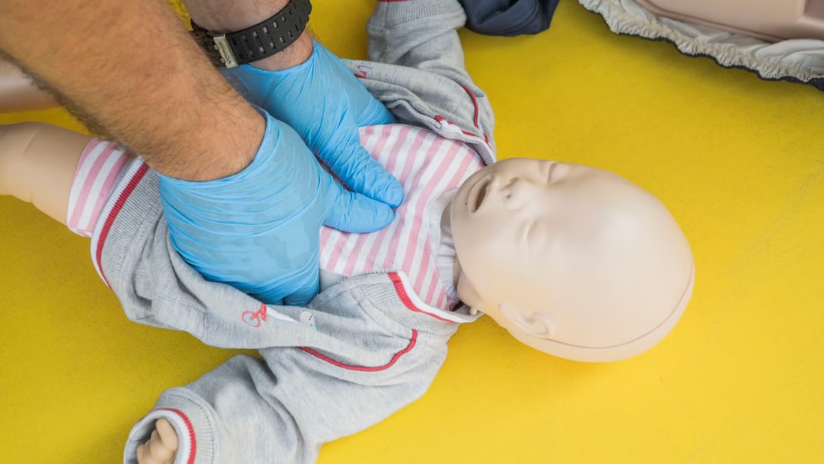 Hands performing CPR on an infant mannequin for a first aid training session.