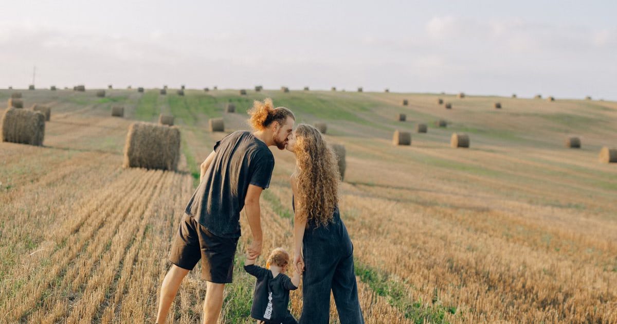 A couple with their child enjoy a sunny day in a wheat field, symbolizing love and joy.