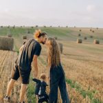 A couple with their child enjoy a sunny day in a wheat field, symbolizing love and joy.