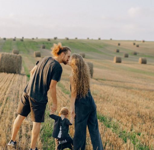 A couple with their child enjoy a sunny day in a wheat field, symbolizing love and joy.